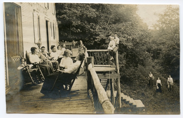 Large family sitting around on the balcony in the Adirondacks. Very old photograph.